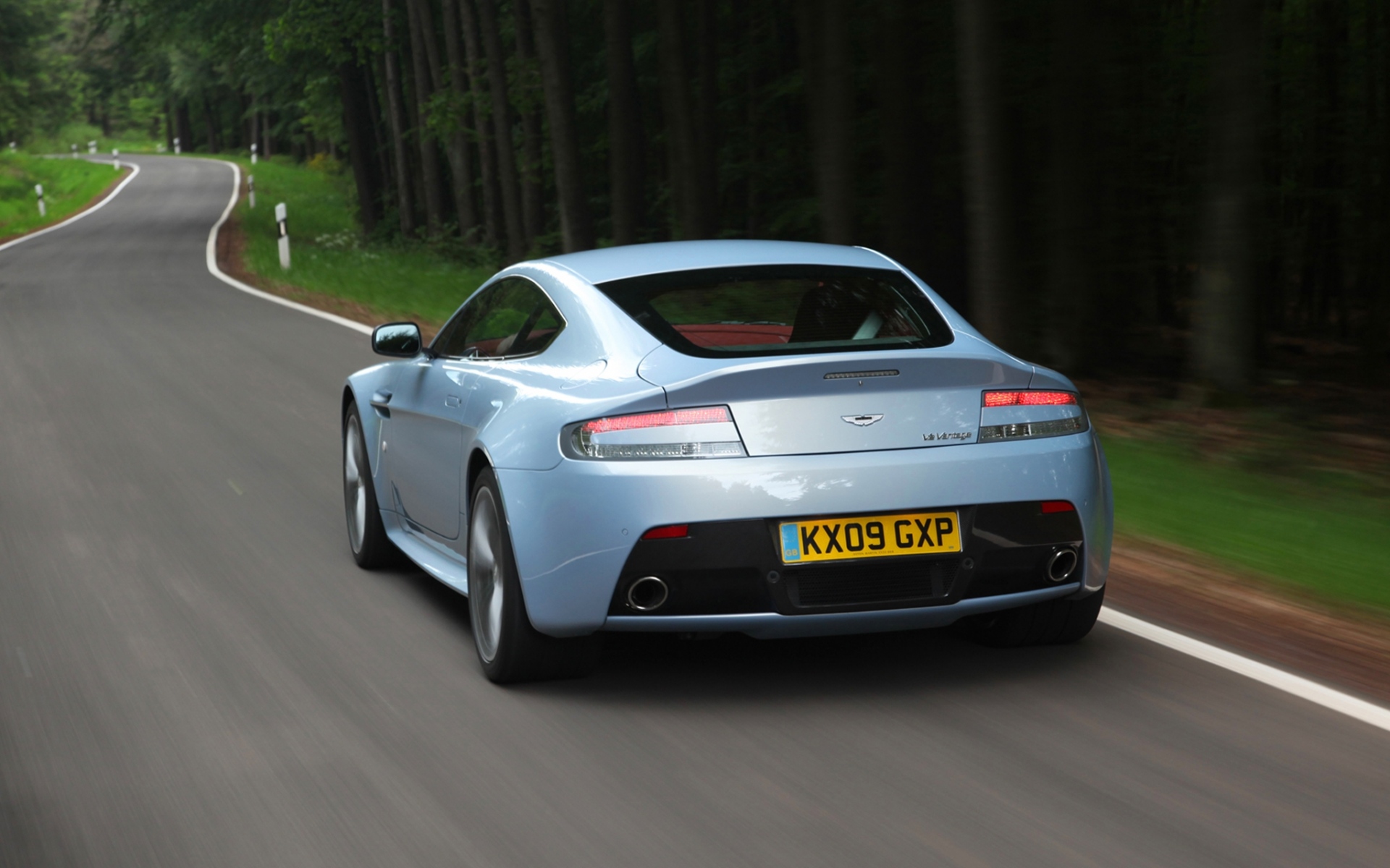 Картинки Aston martin, v12, zagato, 2009, вид сзади, синий металлик, скорость, авто, лес фото и обои на рабочий стол